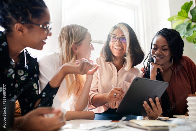 Four women discussing their women-owned small businesses. They are looking at an iPad, while laughing and smiling. They are discussing tax changes. 