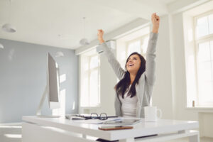 Happy successful smiling business woman raised her hands up while sitting at a table in the office. Successful transaction conclusion of an employment contract successful interview. Success in business work.